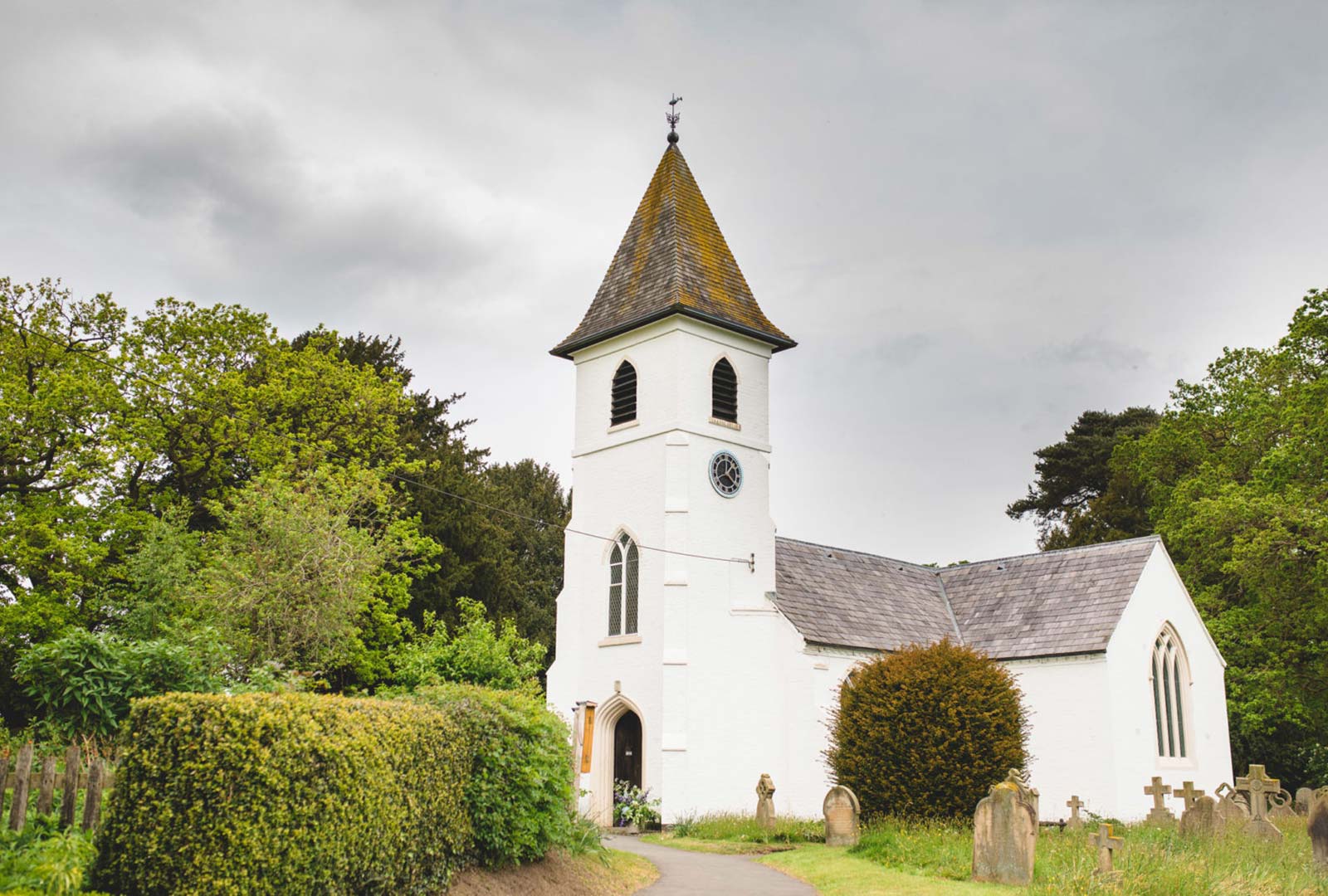 A view of a whitewashed country church set amongst topiary and a countryside environment