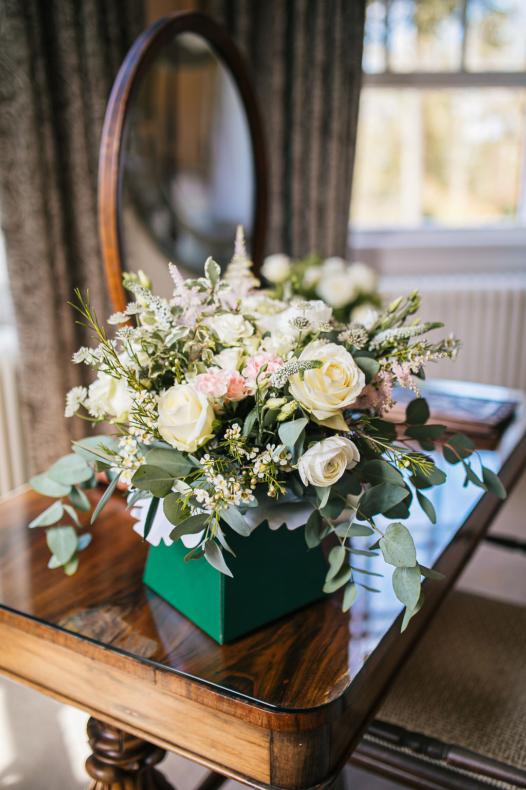 Large bouquet of flowers containing lots of white roses sits on a mahogany dressing table