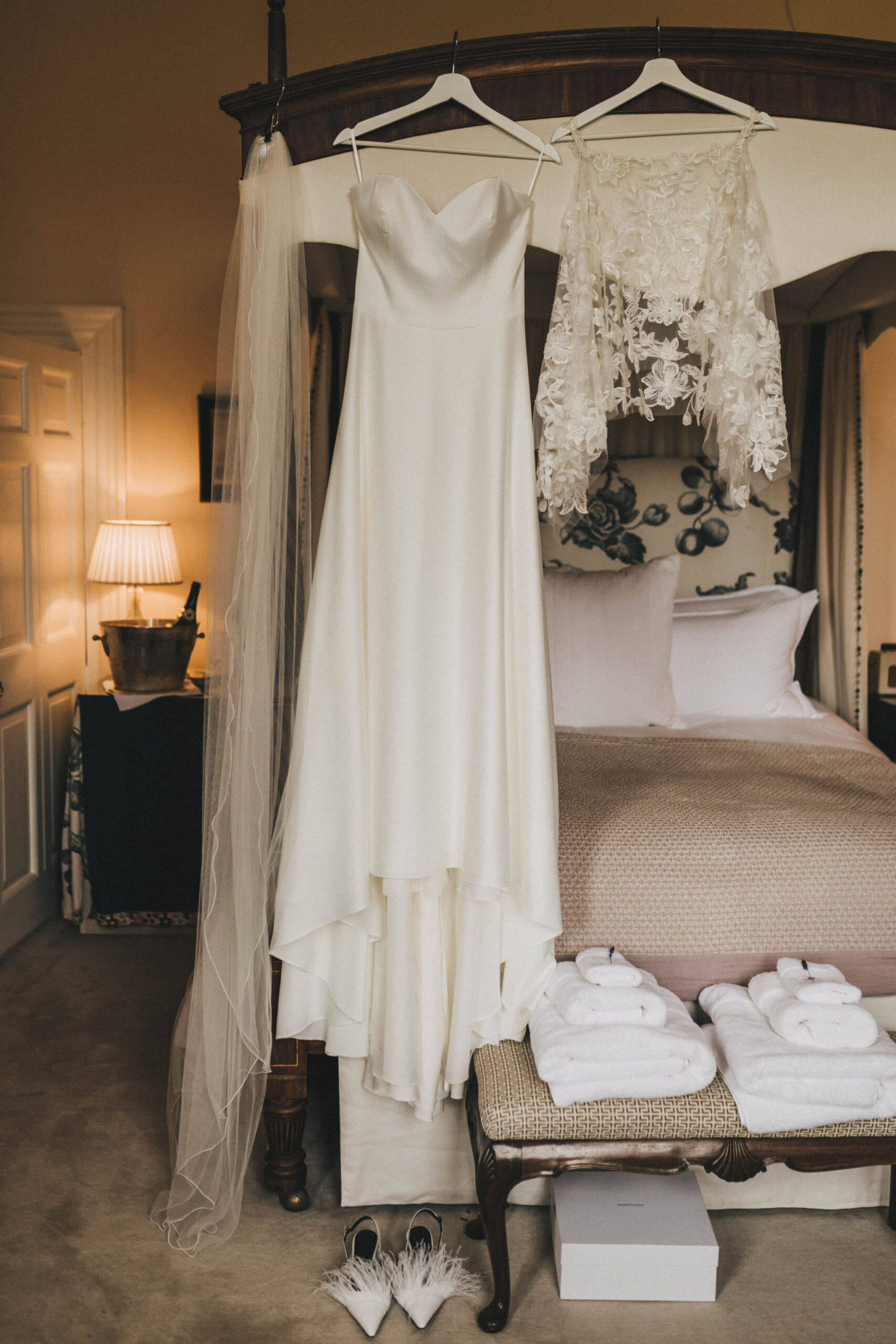 A long silk wedding dress hangs off the edge of an antique wooden four poster bed
