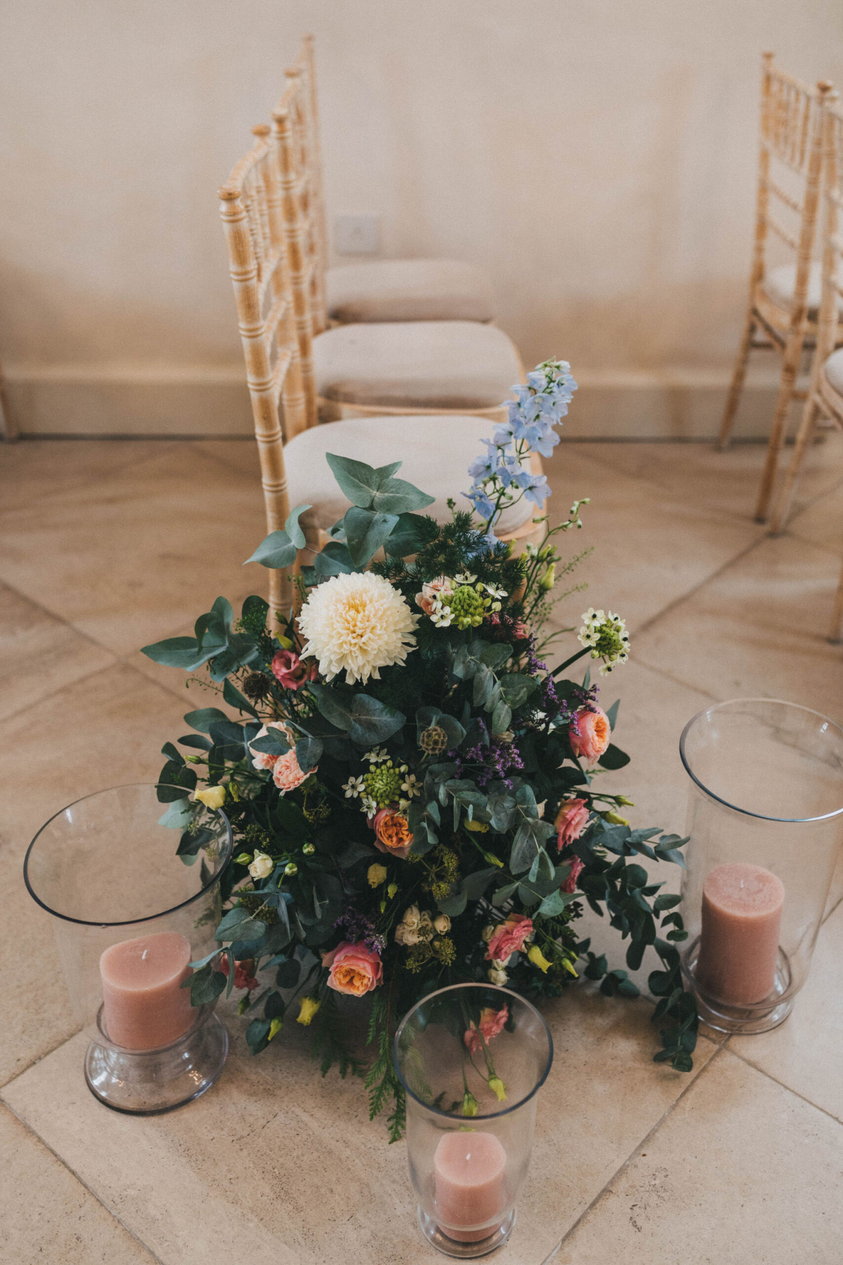 A close up of a floral pew end positioned on the floor makeup of blue, white and orange flowers and foliage