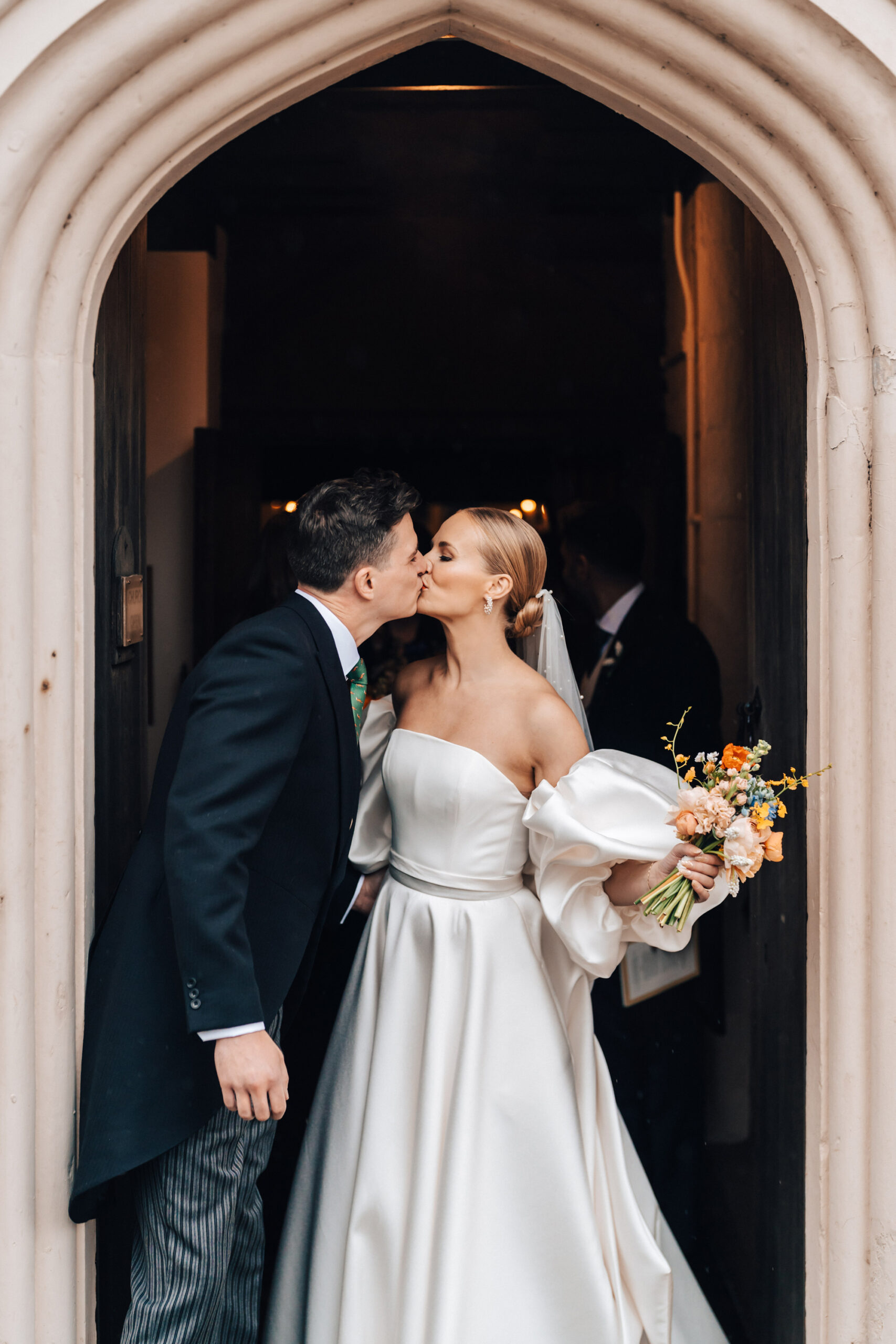 A bride and groom kissing at a church door after getting married