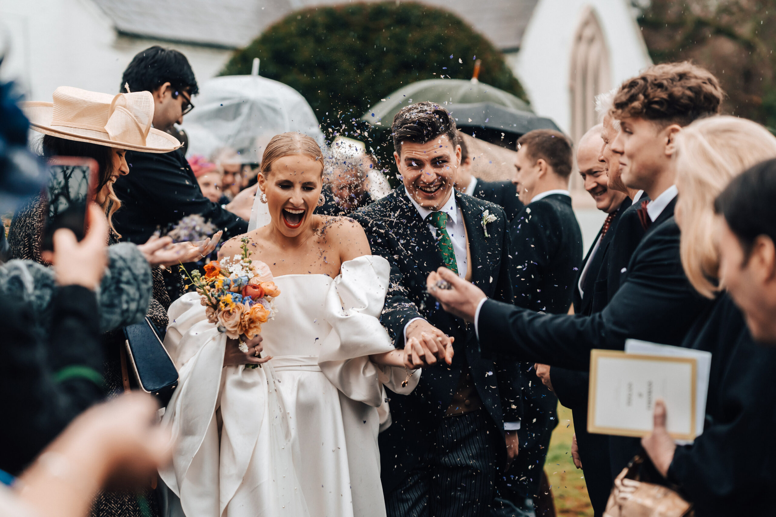 A bride and groom showered in confetti thrown on them by their guests outside a church