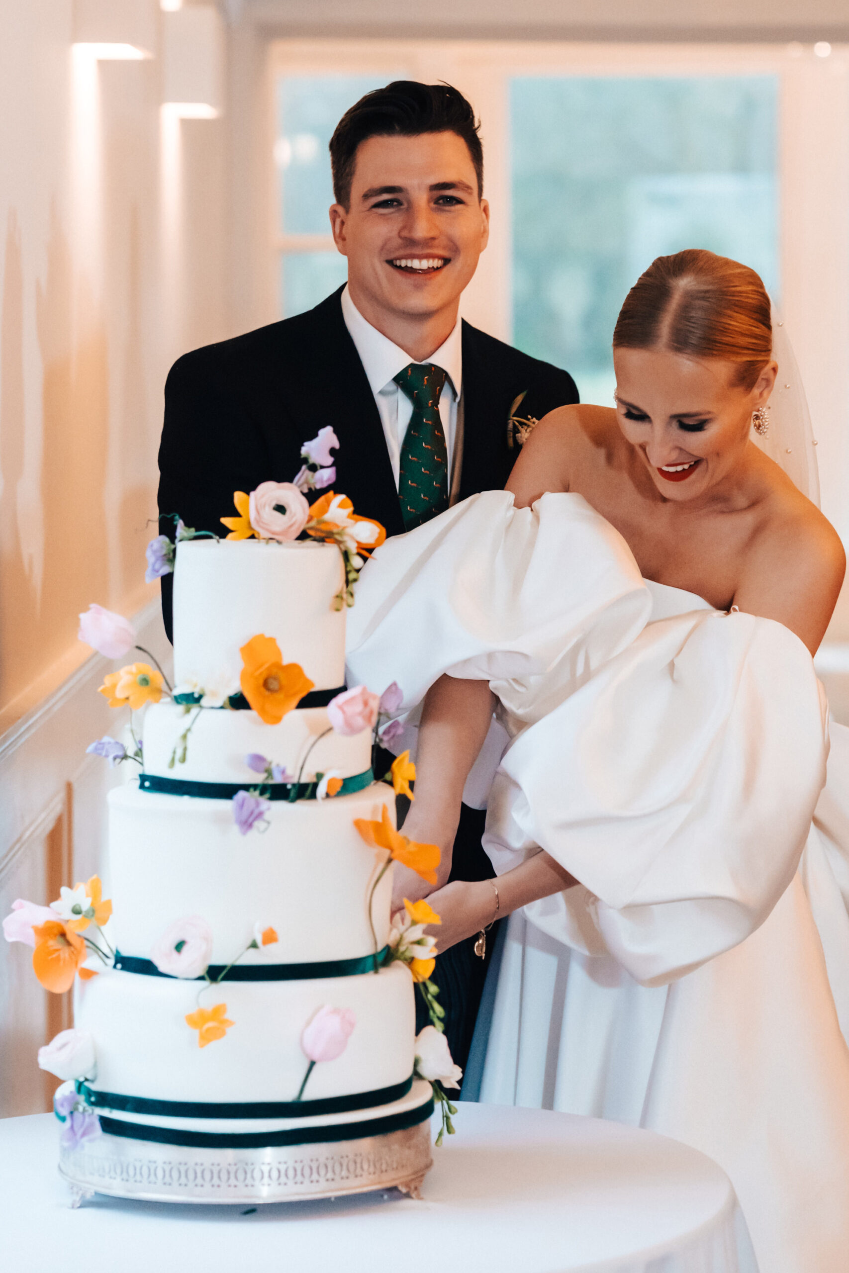 Bride and groom cutting their three tiered wedding cake that is covered with orange sugar flowers and black ribbon detailing