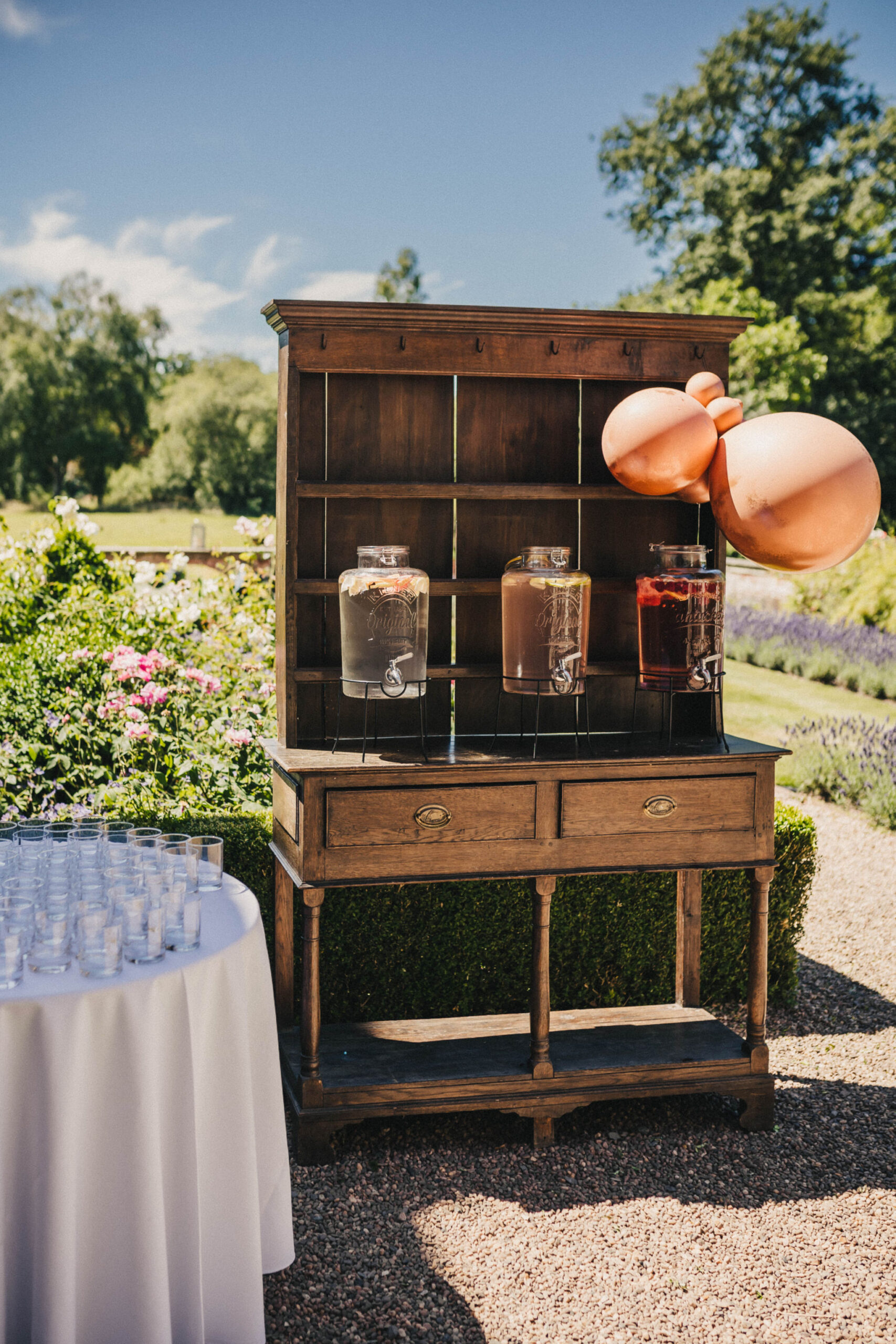 An old welsh wooden dresser has been repurposed as a bar for an outside wedding with glasses set up on it and decanters filled with drinks
