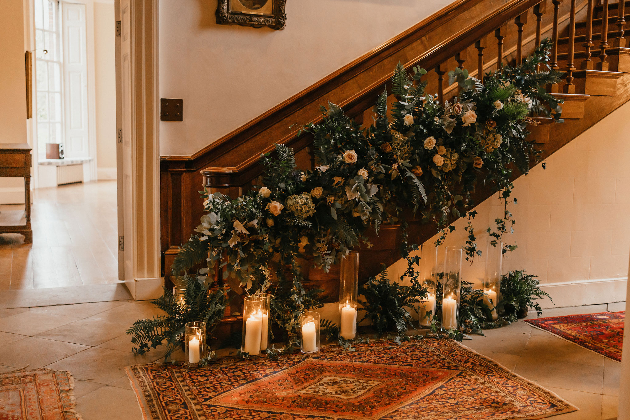 Roses, hydrangeas and peach blossoms mixed with ivy and eucalyptus are entwined around the bannister of a wooden Georgian bannister