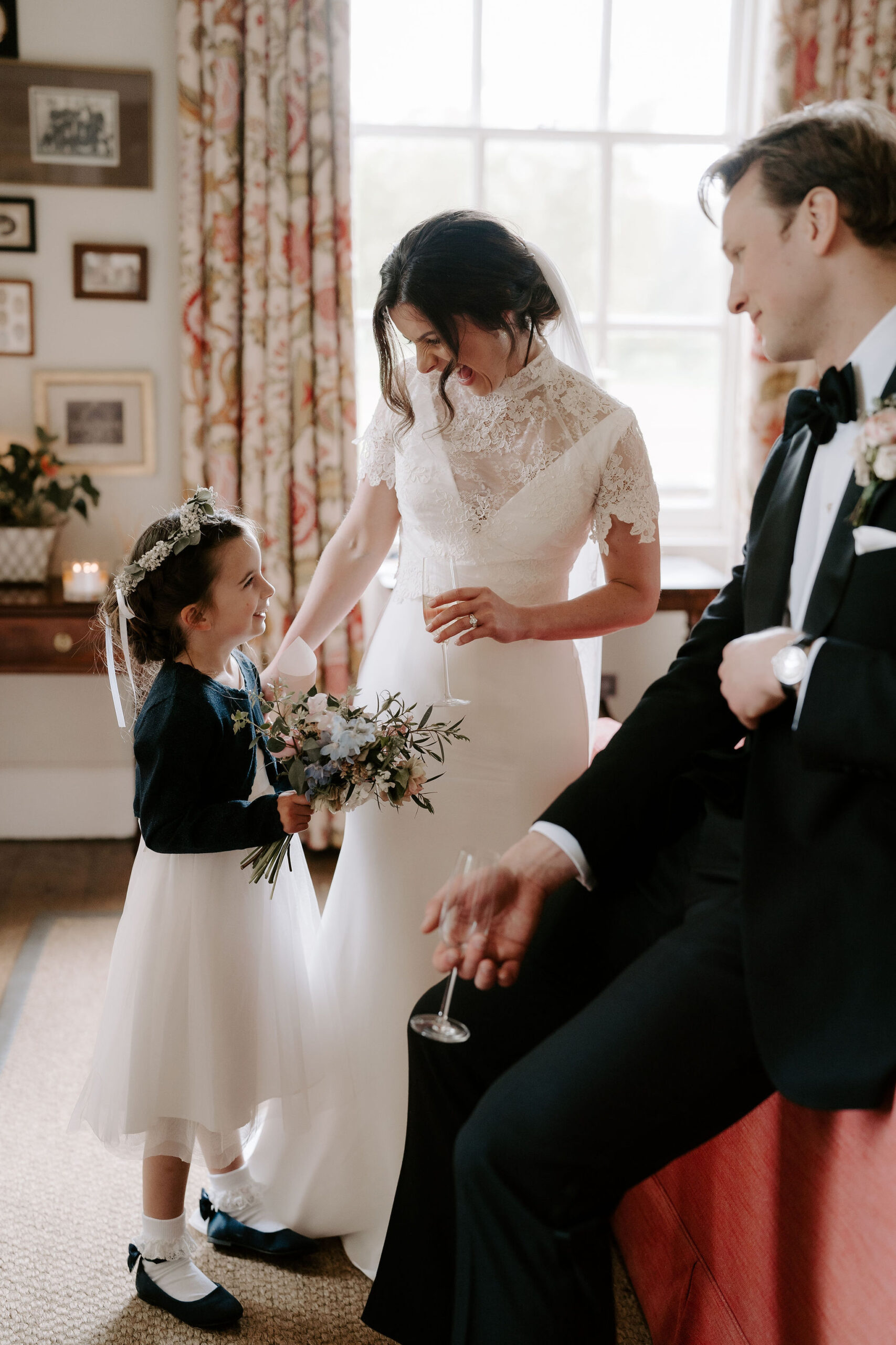 A bride and groom speak to their flower girl who wears a tulle dress and a flower crown in her hair