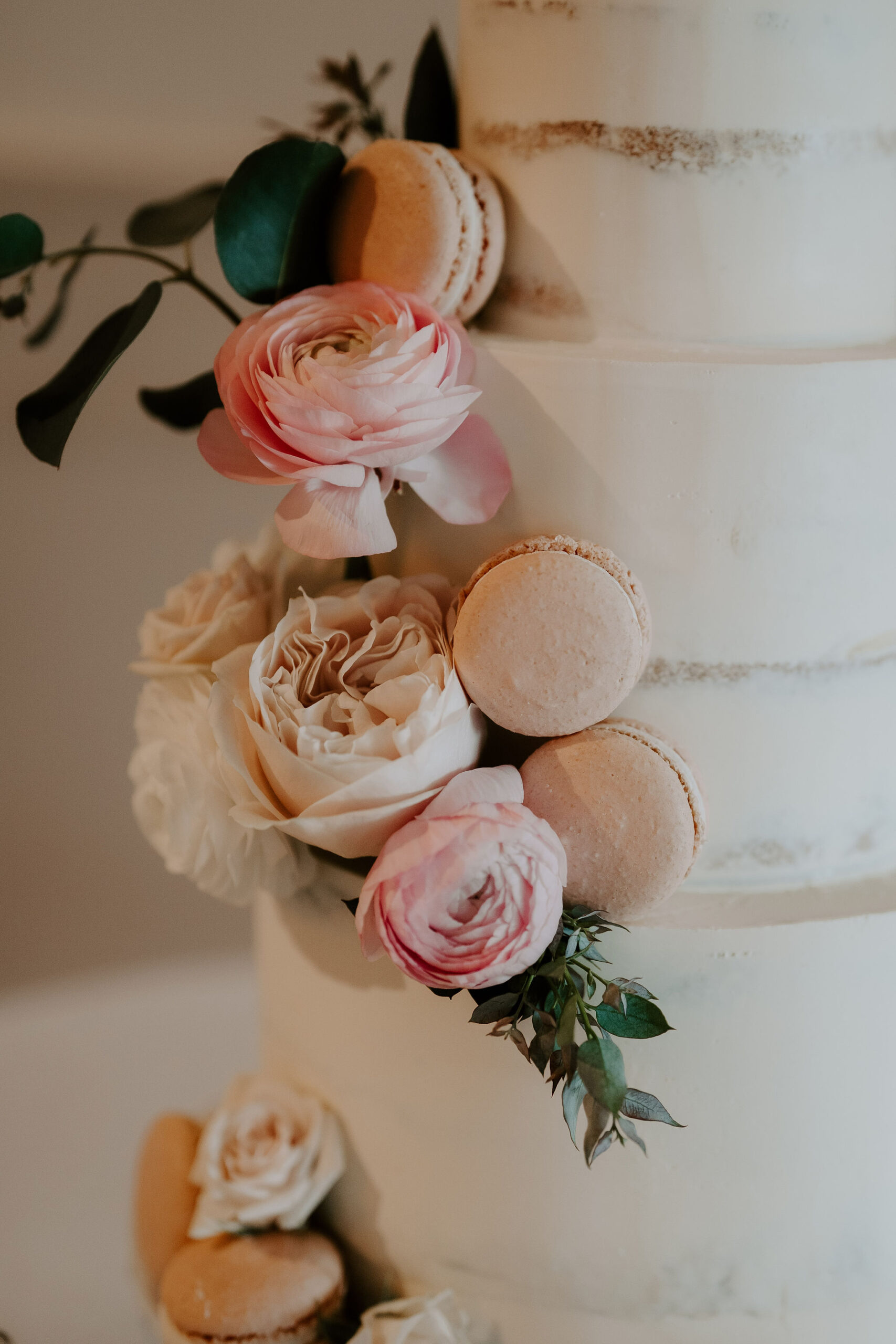 Close up image of a wedding cake with cappuccino and pink toned roses and macarons