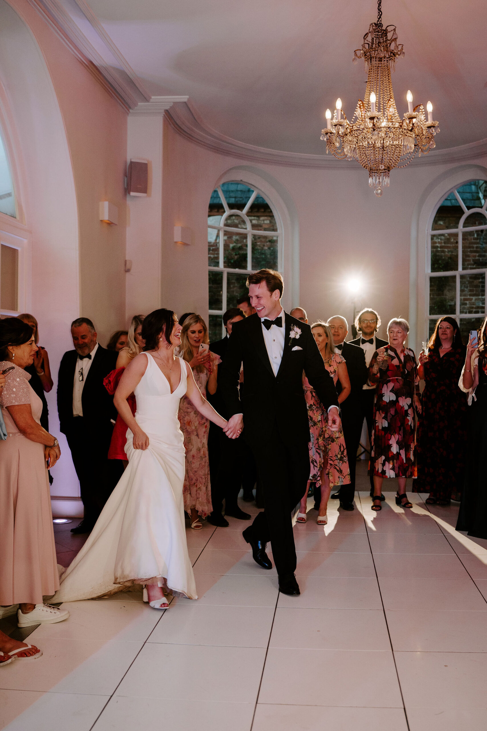 A bride and groom step out onto the dance floor whilst guests congregate around the edges to watch