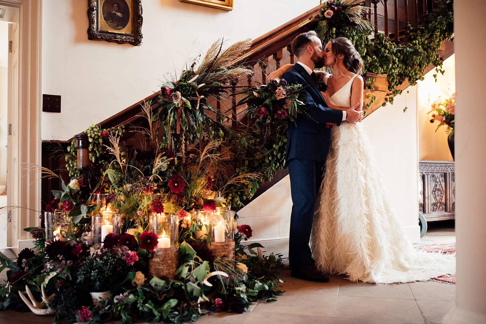 A bride and groom kiss at the bottom of a set of antique wooden stairs surrounded by candles and Autumnal foliage