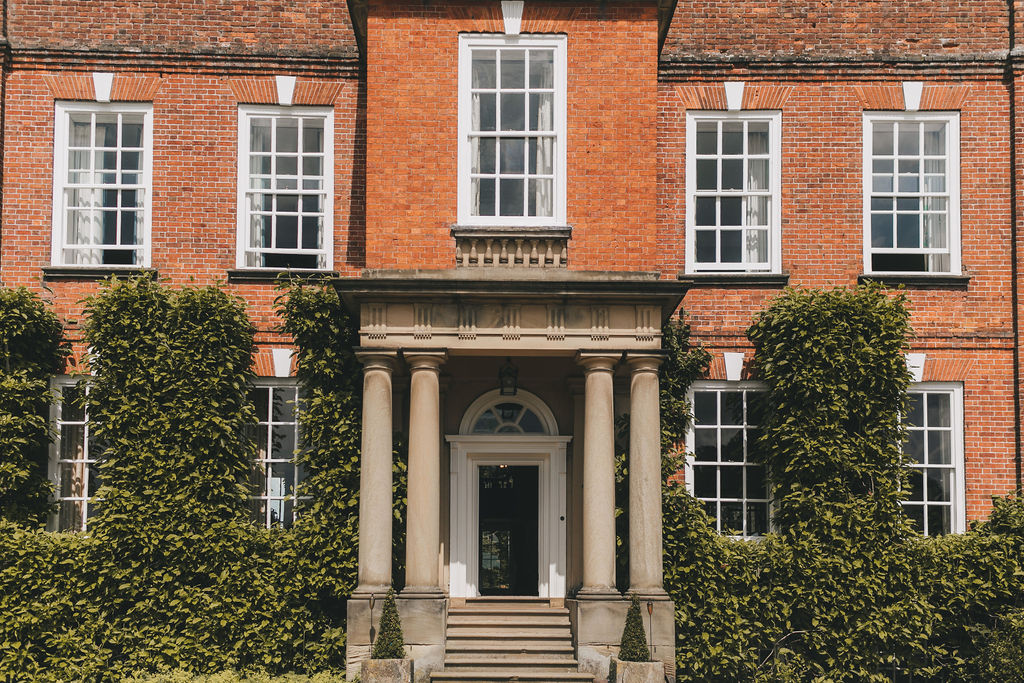 Image of a Georgian Red Brick Mansion from the front of the building with a stone portico, lots of sash large windows and a slate roof set in acres of parkland.