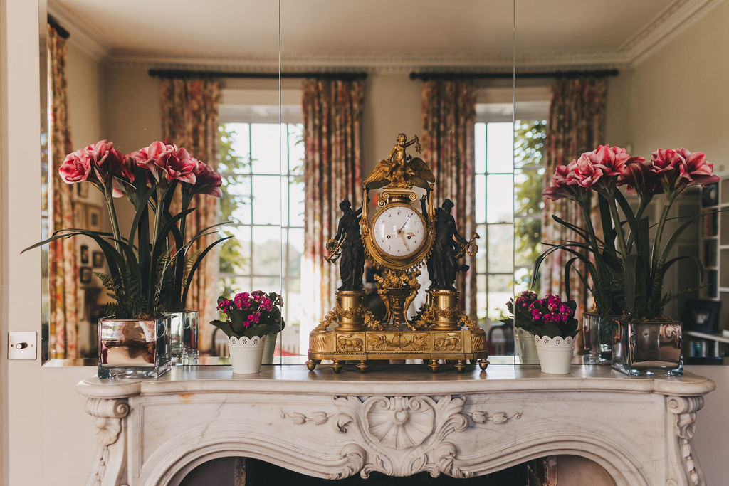 A close up of an ornate marble fireplace with a mirrored glass mantle mirror and carriage clock on the mantlepiece