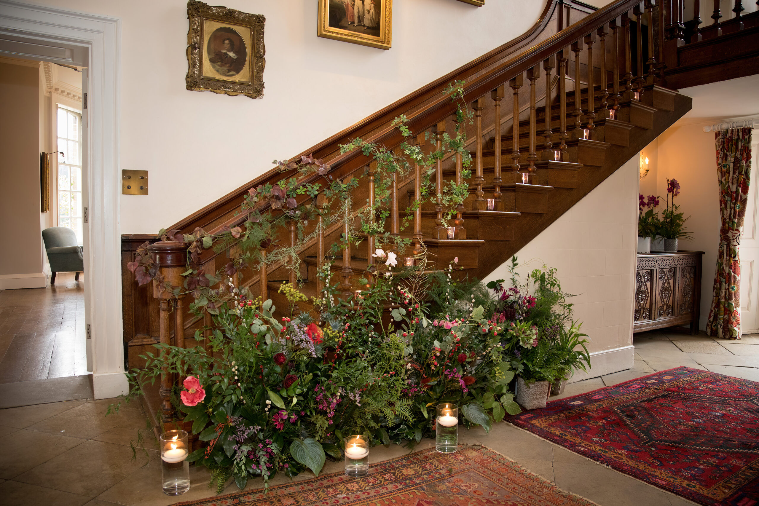 A wooden staircase has been dressed with garlands of ivy and red and berry flower arrangements surround the base of the staircase