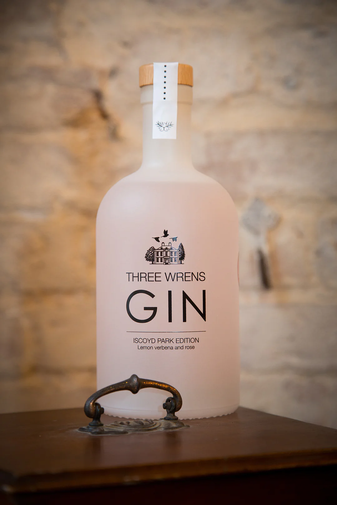 A bottle of Three Wrens Gin in a frosted glass bottle with a light pink hue and an outline of a Georgian Mansion on the bottle