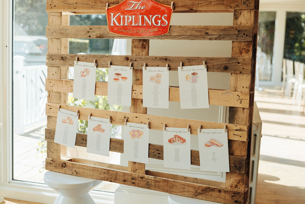 A clever table plan with the theme of Mr Kipling cakes is strung up on a wooden pallet using string and miniature wooden pegs