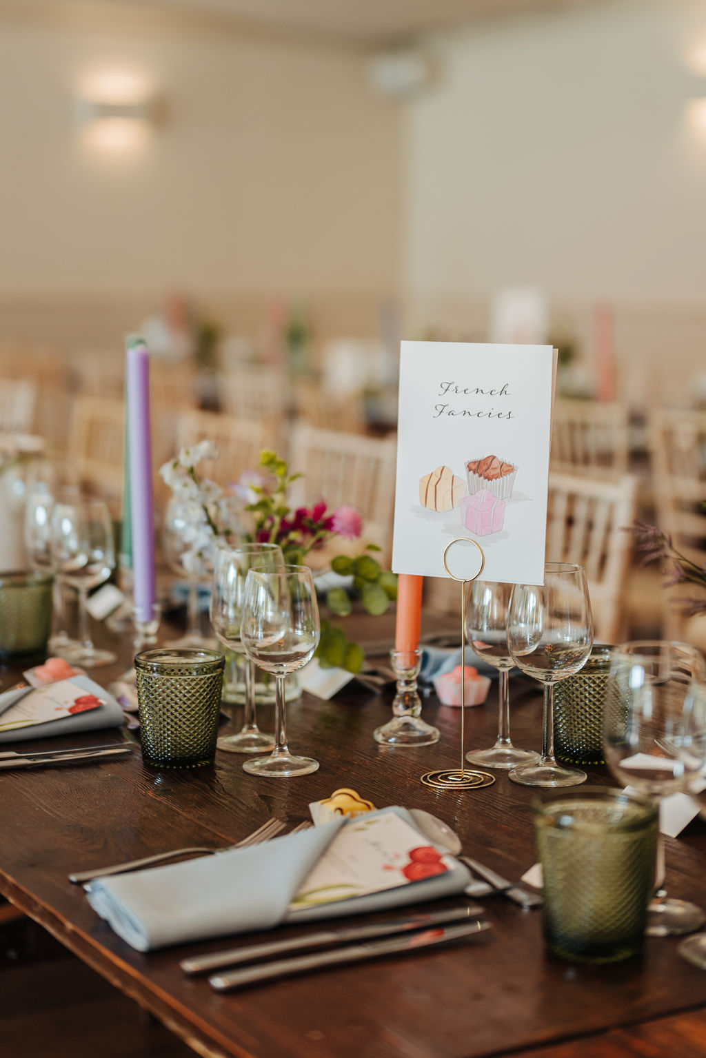 A wedding marquee is set up for a meal with rows of trestle tables on which are lots of pastel toned candles