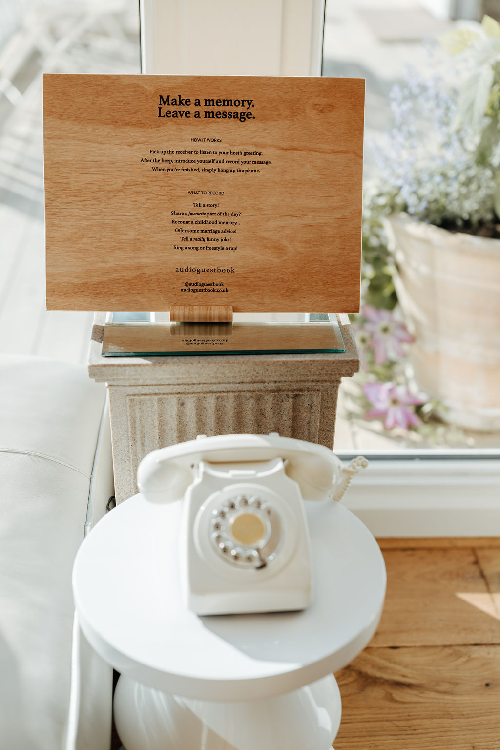 A view of a white telephone on a side table with a wooden sign behind it with instructions on how to leave a message as an alternative wedding guestbook