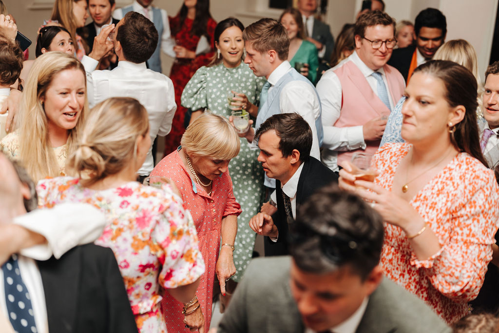 A photograph of lots of wedding guests on the dance floor mingling dancing and chatting