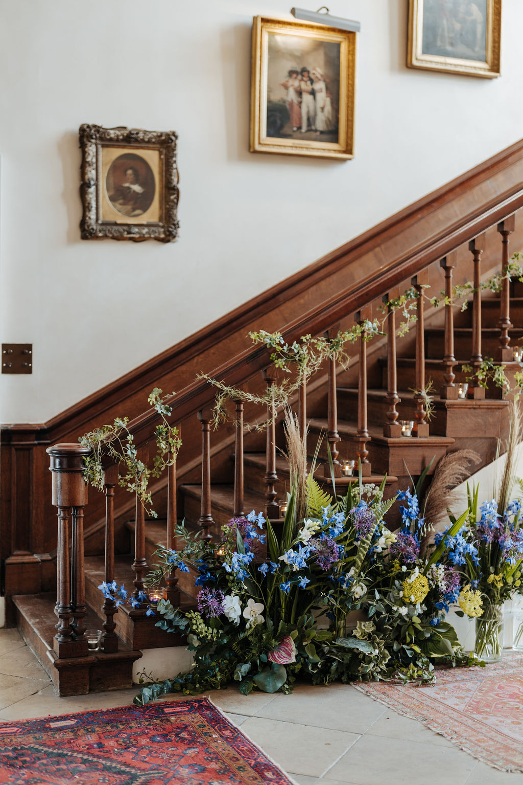 A wooden staircase has been dressed with garlands of ivy and blue and purple flower arrangements surround the base of the staircase