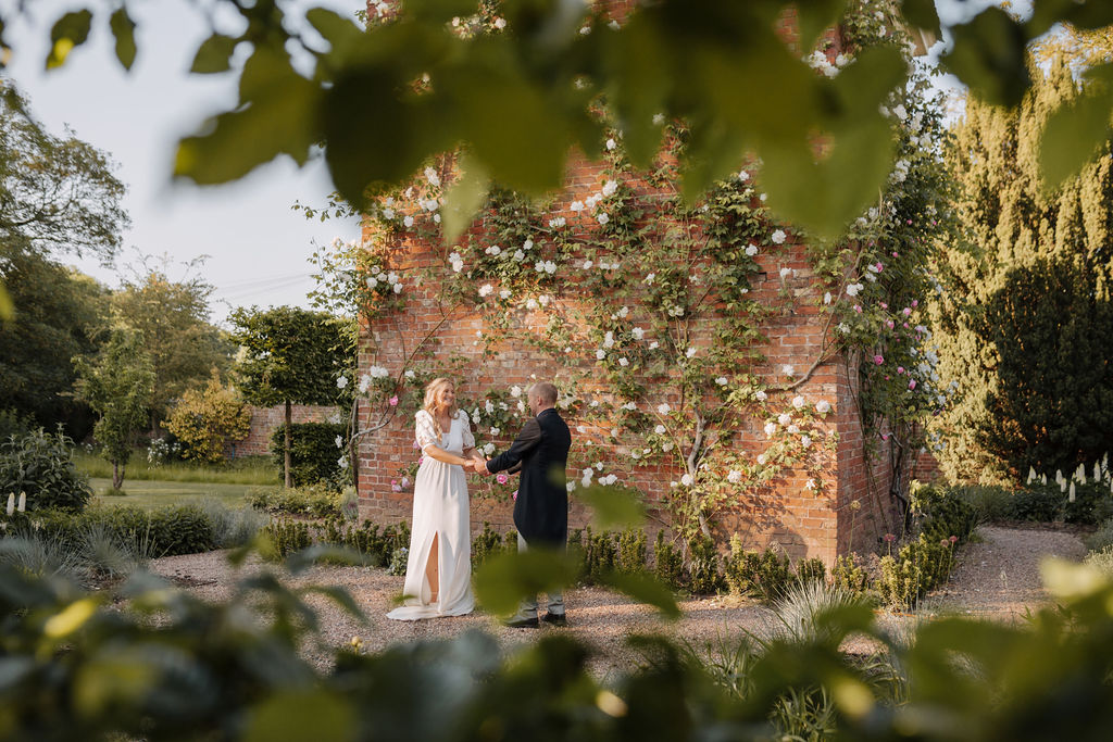 A bride and groom dance unawares outside in a garden surrounded by lots of greenery at the height of Summer