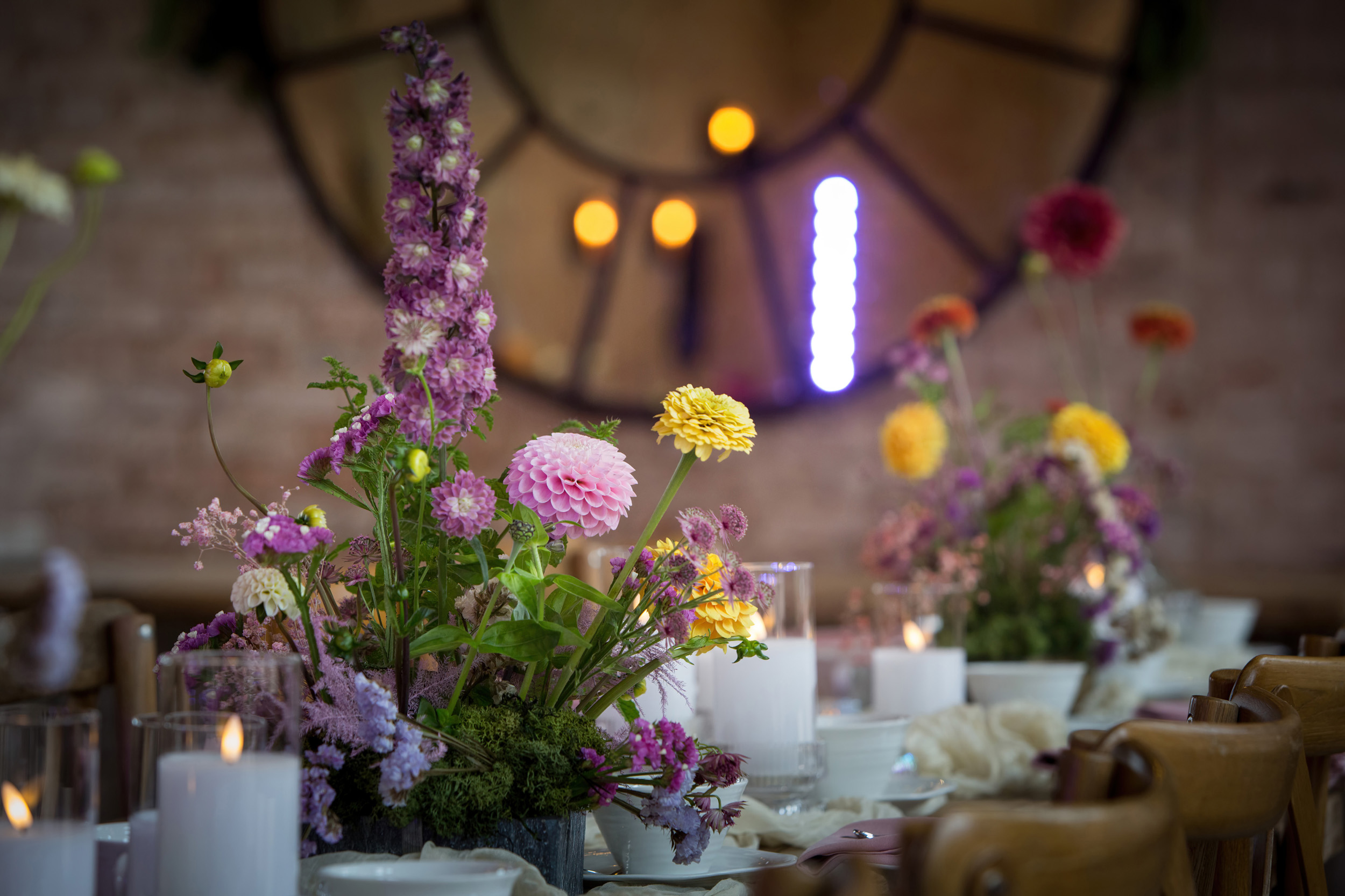 A close up of a floral table arrangement in a yellow and purple colour scheme using dahlias, marigolds and delphiniums