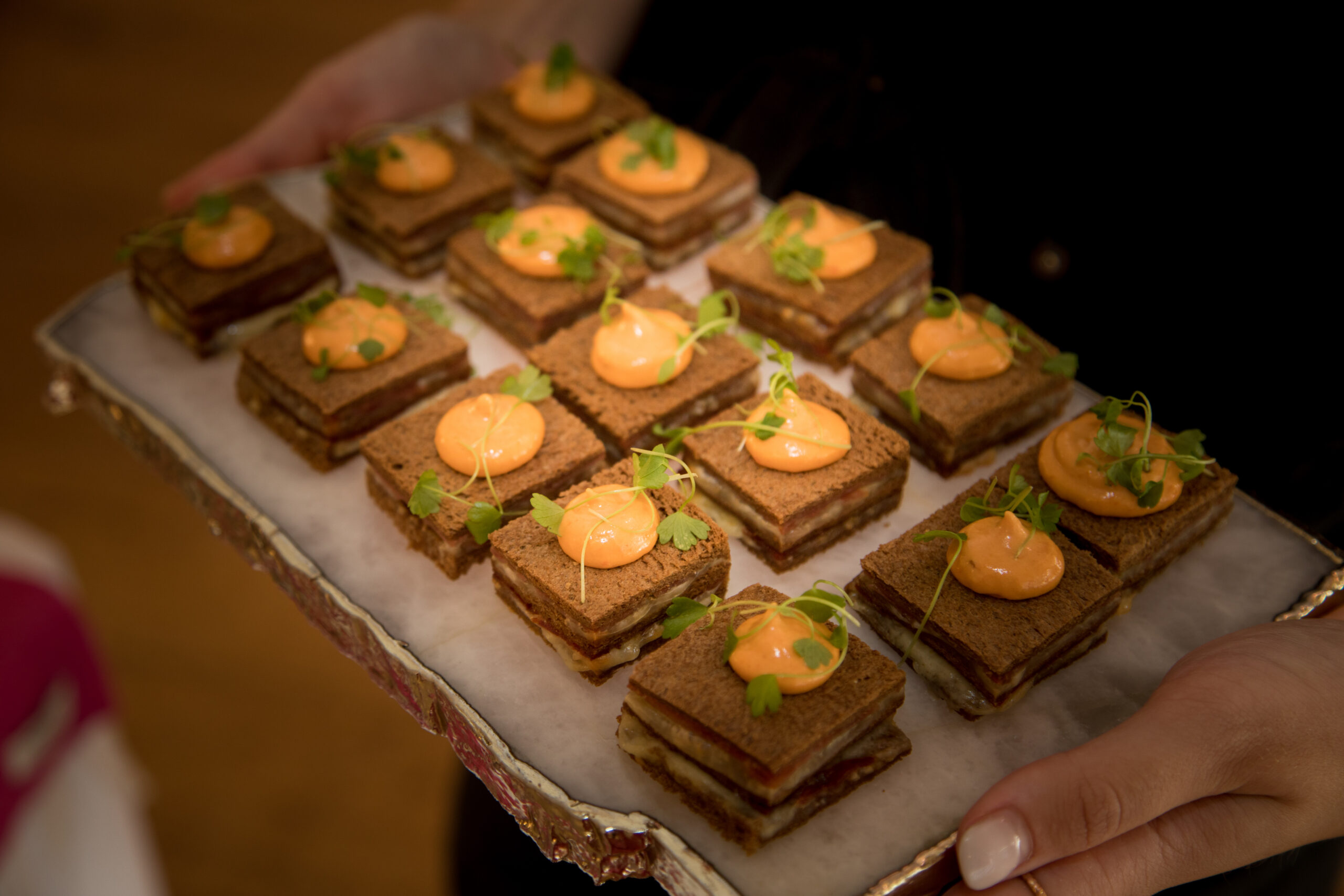 A tray of layered canapés displayed on a quartz gilded edged tray held by a waitress