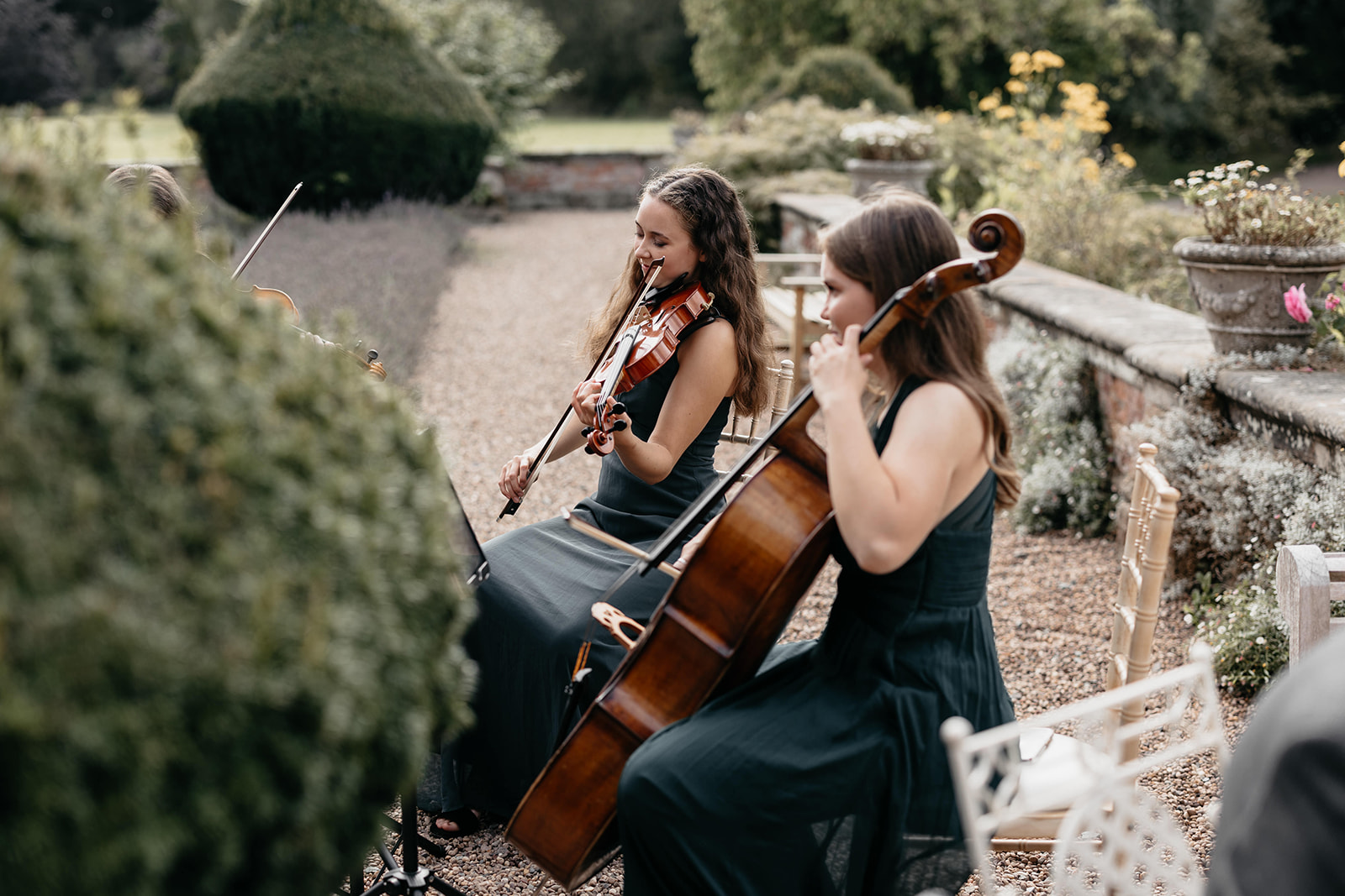 A string quartet of women wearing grey dresses play outside to wedding guests in the summer
