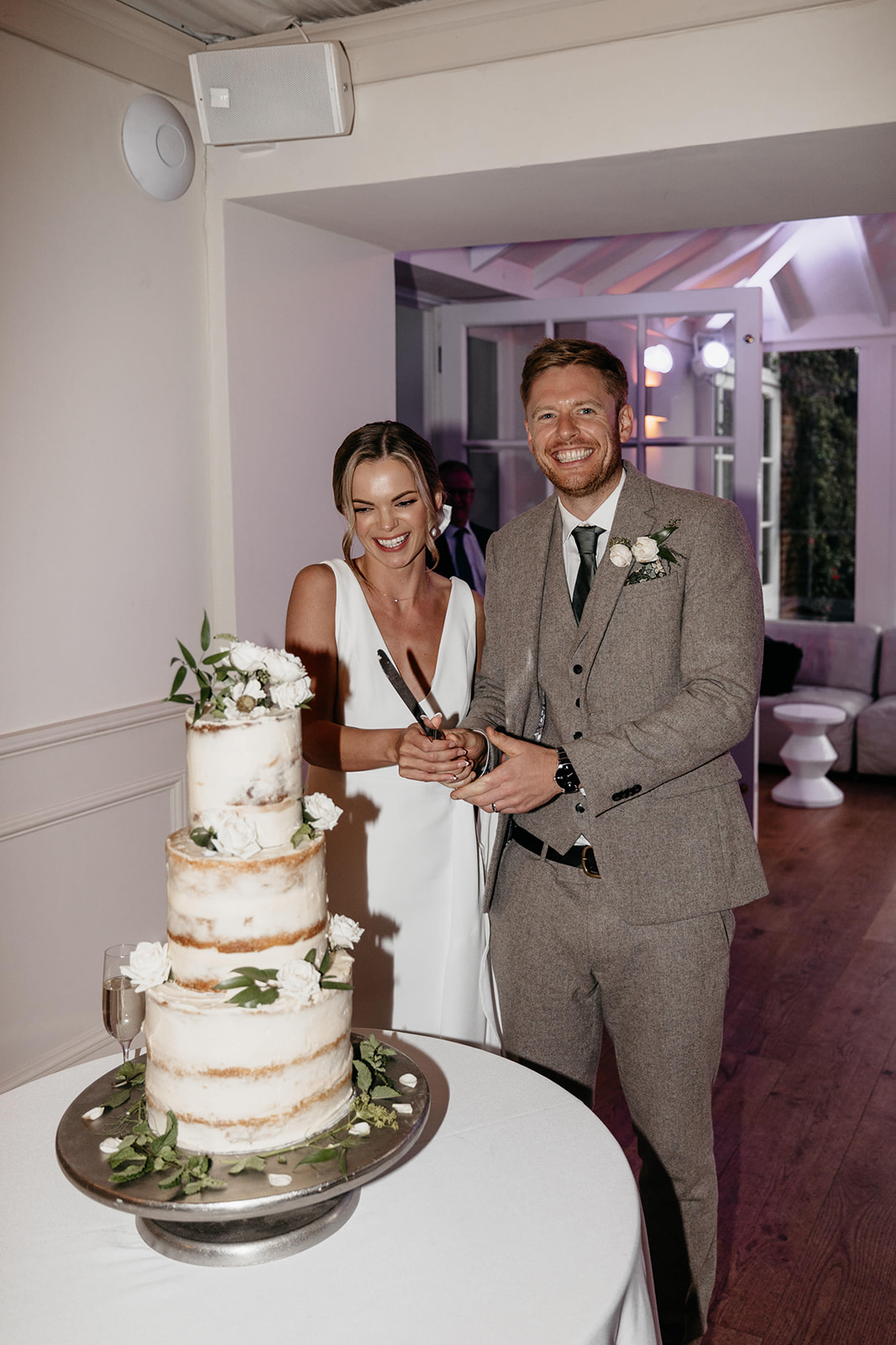 A bride and groom stand behind a three tiered wedding cake holding a cake knife getting ready to cut their cake