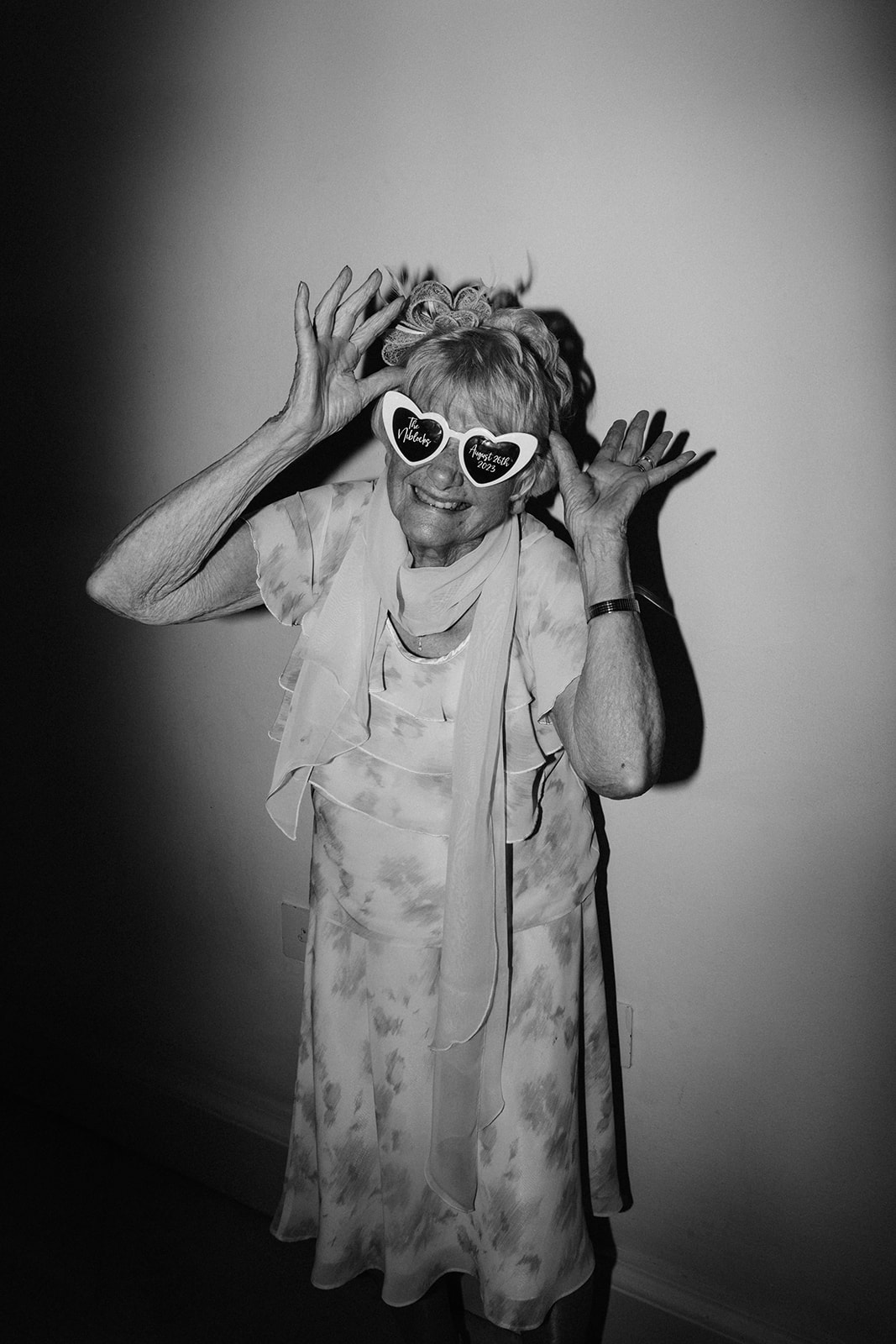 An elderly woman wearing heart shaped glasses poses for the camera